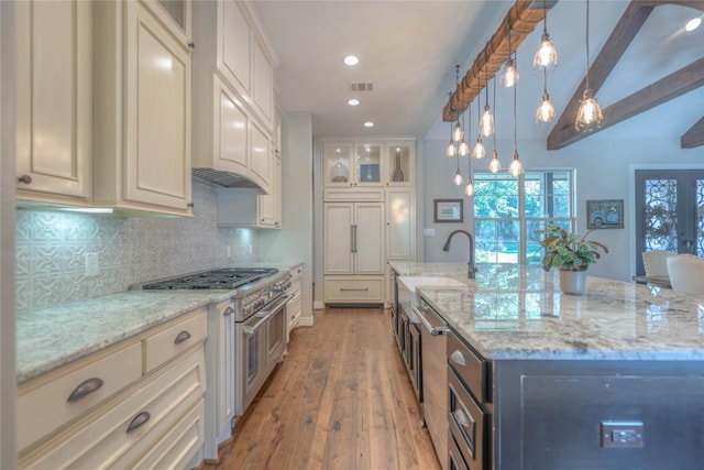 kitchen featuring light stone counters, light hardwood / wood-style floors, decorative light fixtures, range with two ovens, and a kitchen island with sink