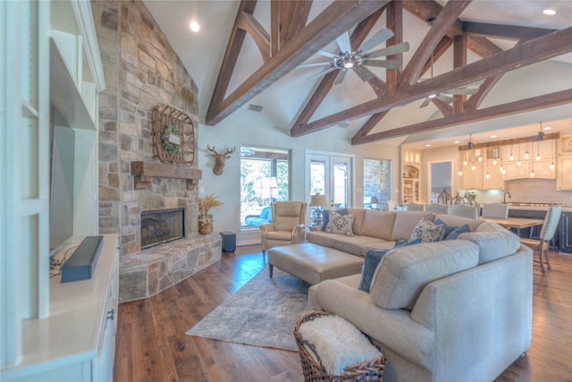 living room featuring hardwood / wood-style flooring, a stone fireplace, beamed ceiling, and high vaulted ceiling