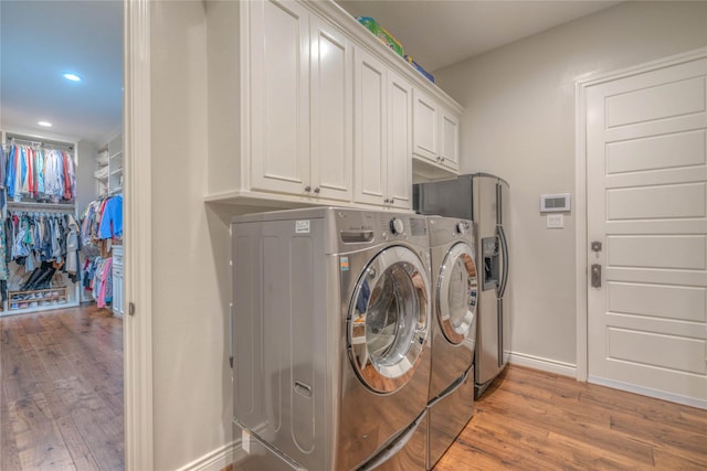 clothes washing area with cabinets, light wood-type flooring, and washing machine and dryer