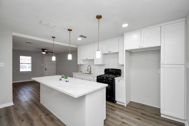 kitchen with black range with gas stovetop, ceiling fan, dark wood-type flooring, a center island, and white cabinetry