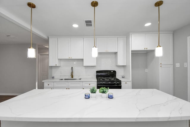 kitchen with black gas range, white cabinetry, light stone counters, decorative light fixtures, and a kitchen island