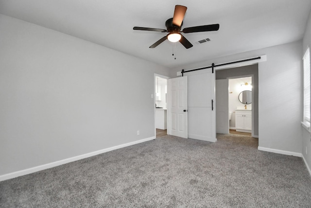 unfurnished bedroom featuring connected bathroom, a barn door, ceiling fan, and carpet flooring