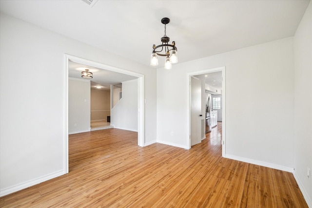 unfurnished room featuring an inviting chandelier and light hardwood / wood-style flooring