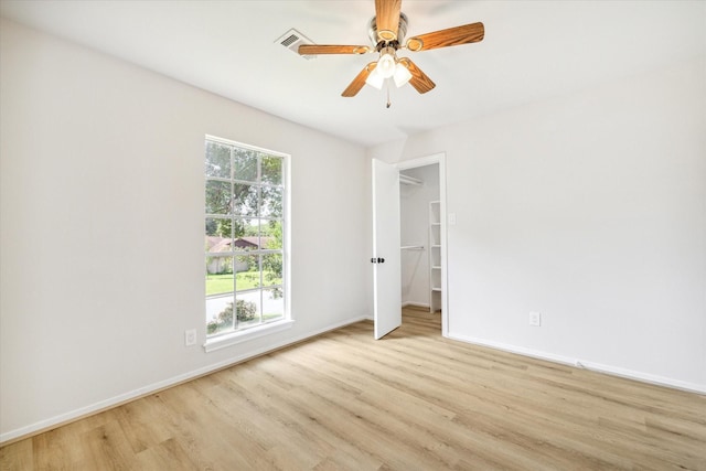 unfurnished bedroom with a closet, a walk in closet, ceiling fan, and light hardwood / wood-style flooring