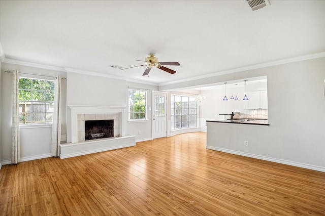 unfurnished living room featuring plenty of natural light, light wood-type flooring, ornamental molding, and a tiled fireplace