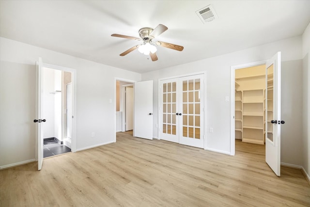 unfurnished bedroom with a walk in closet, ceiling fan, french doors, and light wood-type flooring