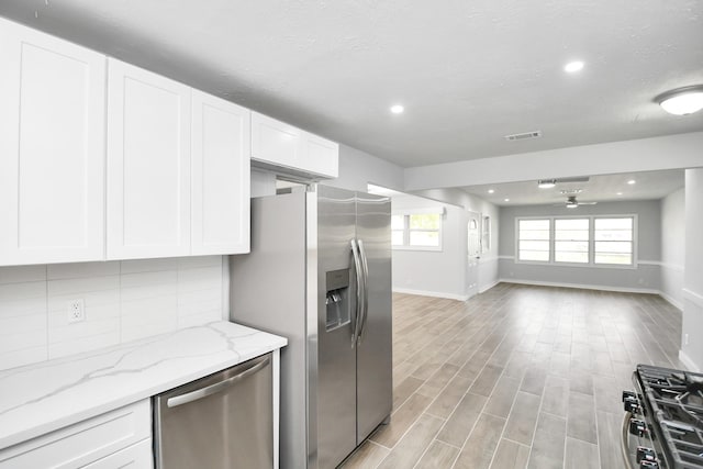 kitchen with light stone counters, backsplash, appliances with stainless steel finishes, white cabinets, and light wood-type flooring