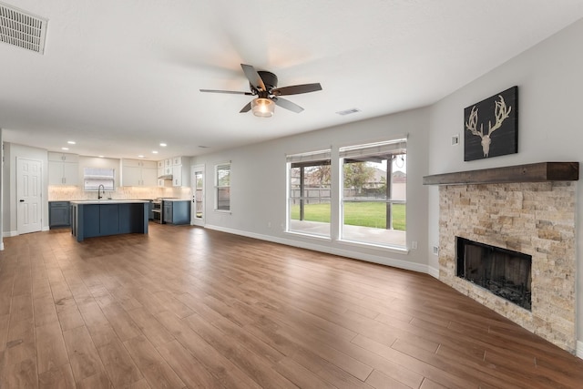 unfurnished living room featuring hardwood / wood-style floors, ceiling fan, sink, and a fireplace