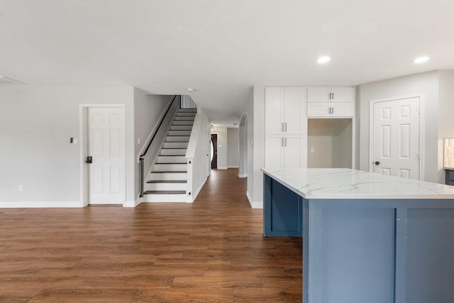 kitchen with white cabinetry, dark hardwood / wood-style flooring, a kitchen island, and light stone counters