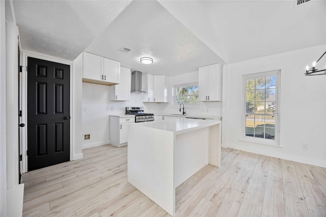 kitchen featuring gas range, a center island, white cabinetry, and wall chimney range hood