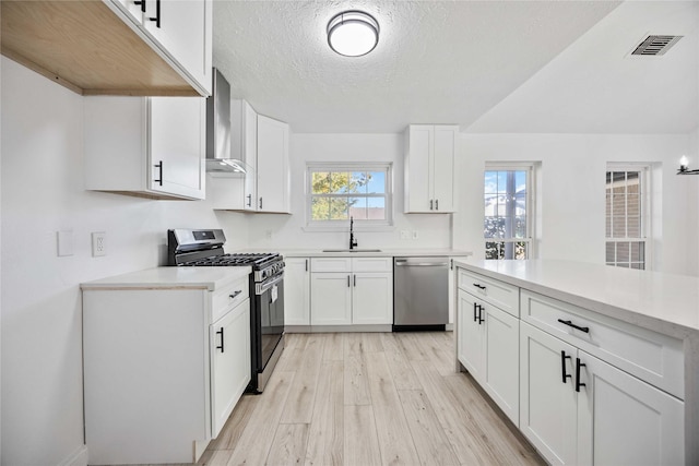 kitchen with appliances with stainless steel finishes, wall chimney exhaust hood, a textured ceiling, light hardwood / wood-style flooring, and white cabinetry