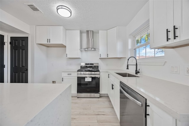 kitchen featuring white cabinets, sink, wall chimney exhaust hood, a textured ceiling, and appliances with stainless steel finishes