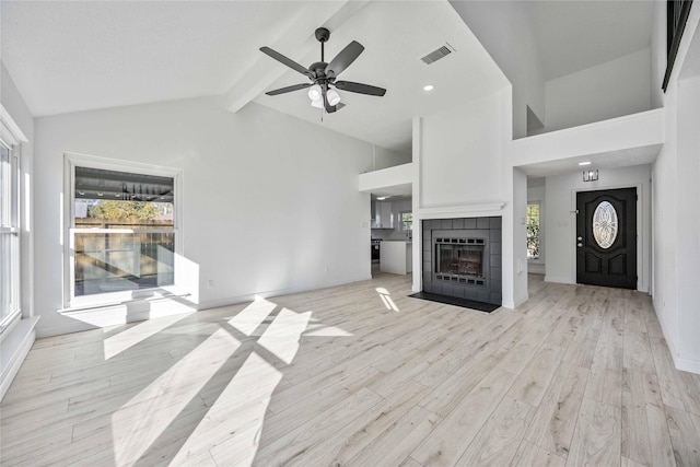 unfurnished living room with a tile fireplace, ceiling fan, light hardwood / wood-style flooring, beamed ceiling, and high vaulted ceiling