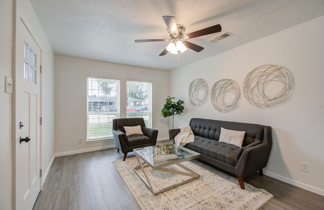 living room with a textured ceiling, ceiling fan, and dark hardwood / wood-style floors