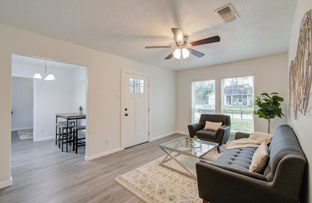 living room featuring ceiling fan with notable chandelier, a textured ceiling, and light hardwood / wood-style flooring