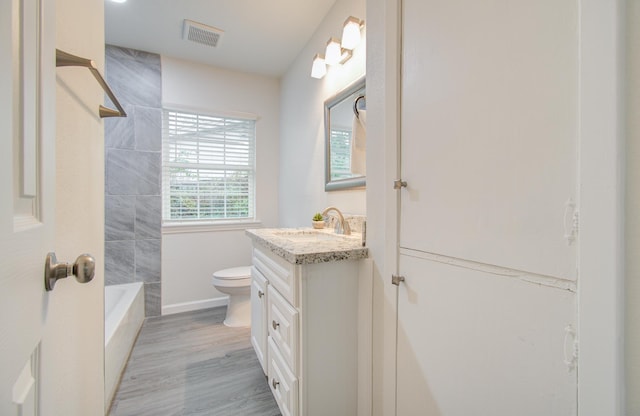 full bathroom with tiled shower / bath, hardwood / wood-style flooring, vanity, and toilet