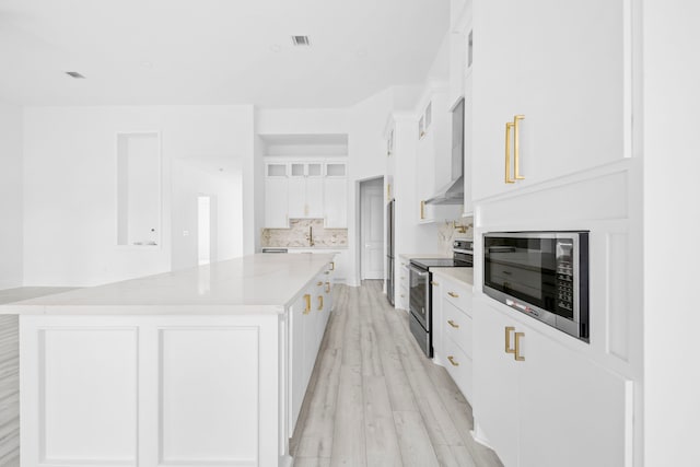 kitchen featuring white cabinetry, light hardwood / wood-style flooring, stainless steel appliances, and a large island