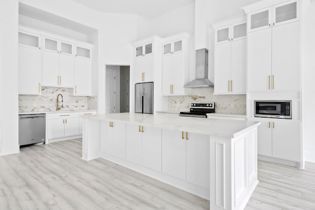 kitchen featuring white cabinets, a center island, wall chimney exhaust hood, and appliances with stainless steel finishes