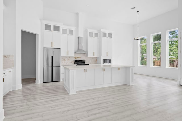 kitchen featuring wall chimney exhaust hood, stainless steel appliances, a kitchen island with sink, light hardwood / wood-style flooring, and white cabinets