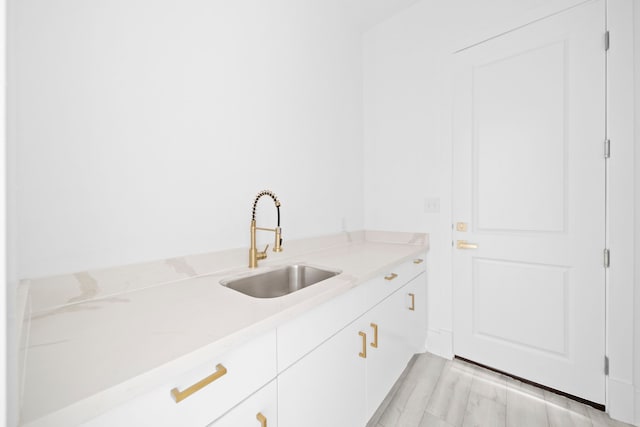 kitchen featuring light stone counters, light hardwood / wood-style floors, white cabinetry, and sink