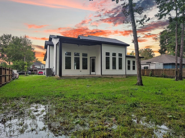 back house at dusk featuring a lawn and central AC