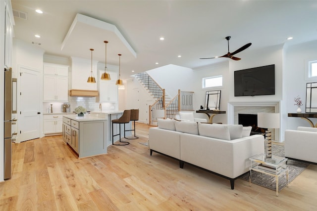 living room featuring a premium fireplace, crown molding, ceiling fan, and light wood-type flooring