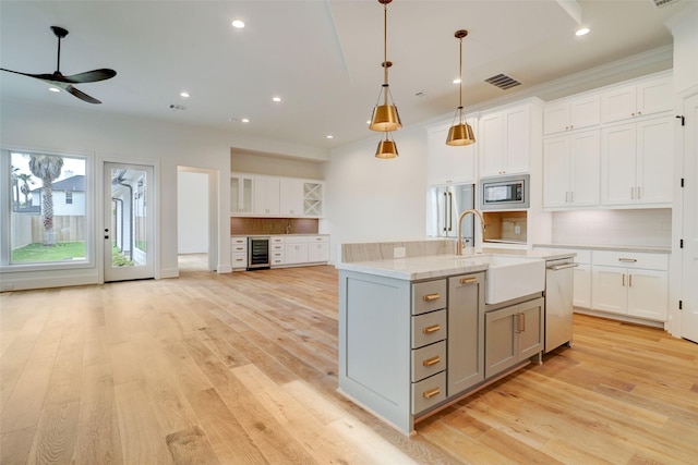 kitchen featuring pendant lighting, light wood-type flooring, appliances with stainless steel finishes, white cabinetry, and beverage cooler