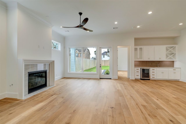 unfurnished living room featuring ornamental molding, beverage cooler, ceiling fan, a fireplace, and light hardwood / wood-style floors