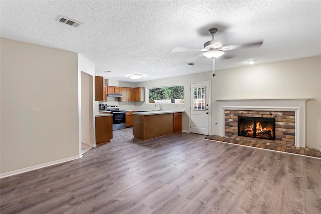 kitchen featuring kitchen peninsula, a brick fireplace, a textured ceiling, wood-type flooring, and stainless steel range with electric cooktop