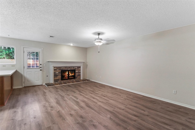 unfurnished living room with hardwood / wood-style floors, ceiling fan, a stone fireplace, and a textured ceiling