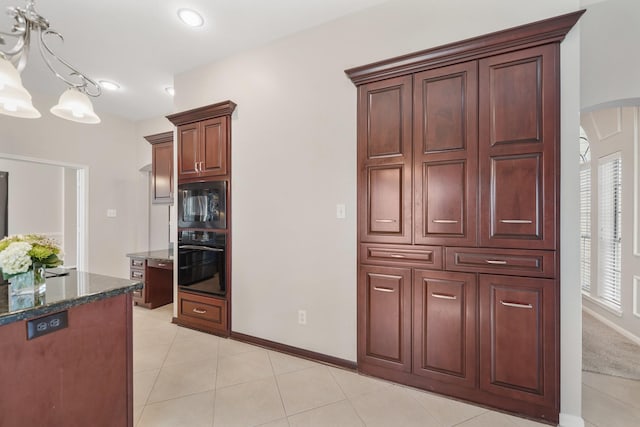 kitchen with built in microwave, a notable chandelier, dark stone countertops, black oven, and light tile patterned floors