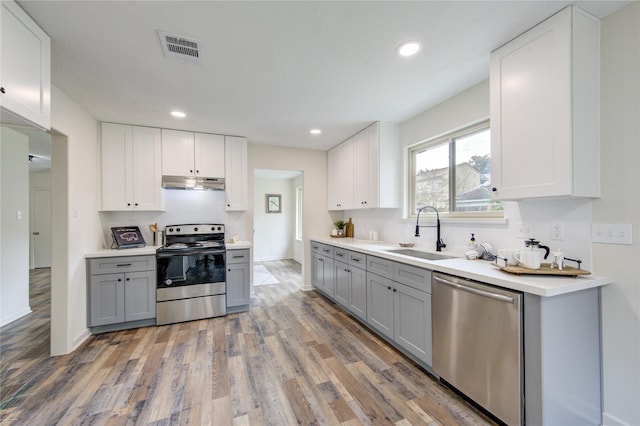 kitchen with gray cabinetry, white cabinetry, sink, stainless steel appliances, and hardwood / wood-style flooring