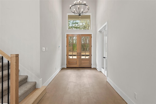 foyer entrance featuring light wood-type flooring, french doors, a towering ceiling, and a chandelier