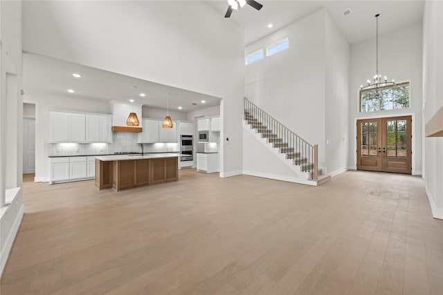 unfurnished living room with french doors, ceiling fan with notable chandelier, light hardwood / wood-style floors, and a high ceiling