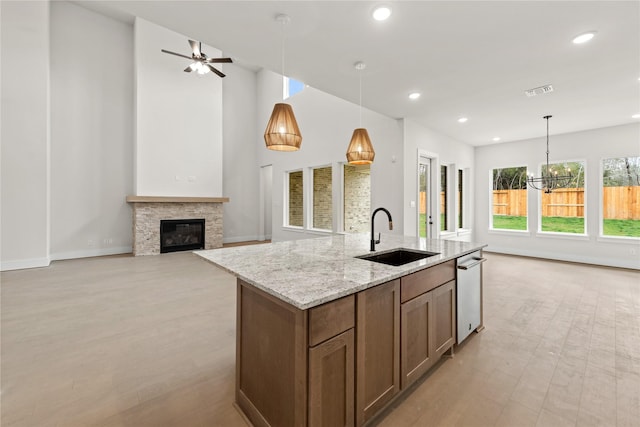 kitchen with light stone countertops, sink, pendant lighting, a center island with sink, and a stone fireplace