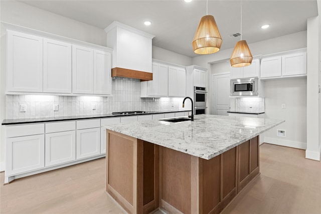 kitchen featuring white cabinetry, sink, decorative light fixtures, a center island with sink, and appliances with stainless steel finishes