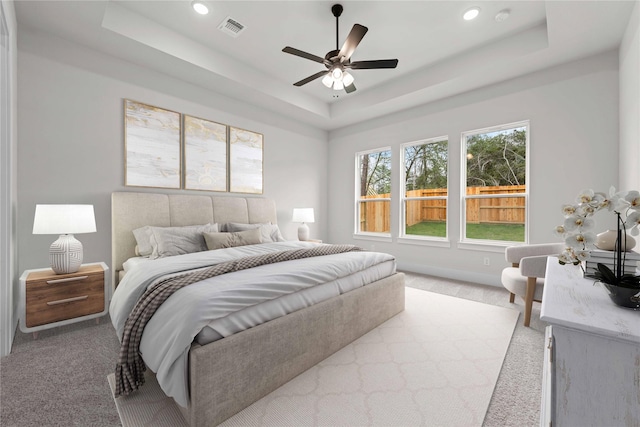 carpeted bedroom featuring ceiling fan and a tray ceiling