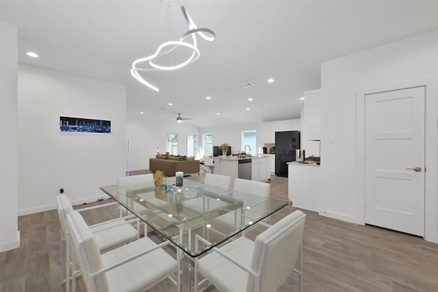 dining room with sink, light hardwood / wood-style floors, and ceiling fan with notable chandelier