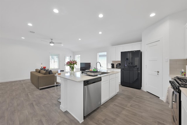 kitchen with light wood-type flooring, stainless steel appliances, ceiling fan, white cabinets, and an island with sink