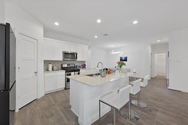 kitchen with appliances with stainless steel finishes, sink, a center island with sink, white cabinets, and light hardwood / wood-style floors