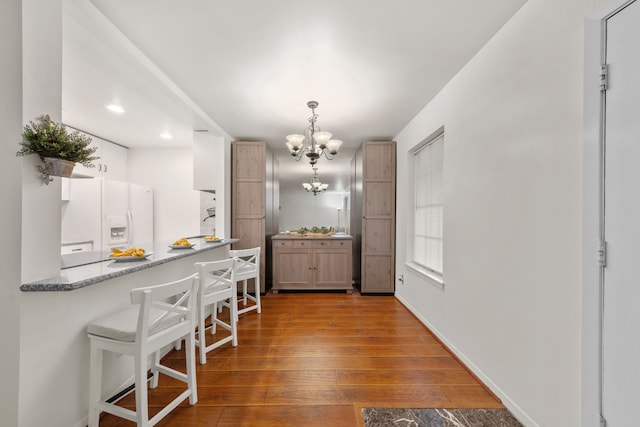 kitchen featuring a notable chandelier, decorative light fixtures, dark hardwood / wood-style flooring, and white refrigerator with ice dispenser