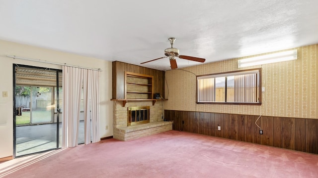 unfurnished living room with ceiling fan, carpet floors, wooden walls, and a brick fireplace