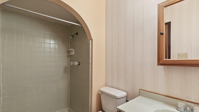 bathroom featuring a tile shower, vanity, and toilet