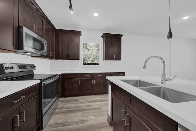 kitchen featuring light stone countertops, sink, pendant lighting, appliances with stainless steel finishes, and light wood-type flooring