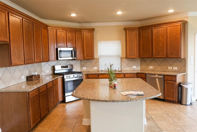 kitchen featuring appliances with stainless steel finishes, crown molding, light stone countertops, and a kitchen island