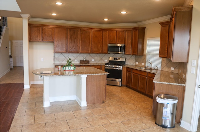 kitchen with appliances with stainless steel finishes, light stone countertops, ornamental molding, decorative backsplash, and a kitchen island