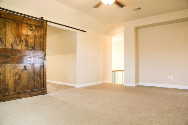 carpeted empty room featuring lofted ceiling, ceiling fan, and a barn door