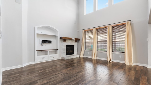 unfurnished living room featuring built in shelves, a towering ceiling, dark wood-type flooring, and a wealth of natural light