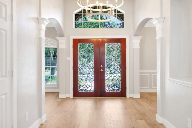 entrance foyer with ornate columns, french doors, a high ceiling, a notable chandelier, and light hardwood / wood-style floors