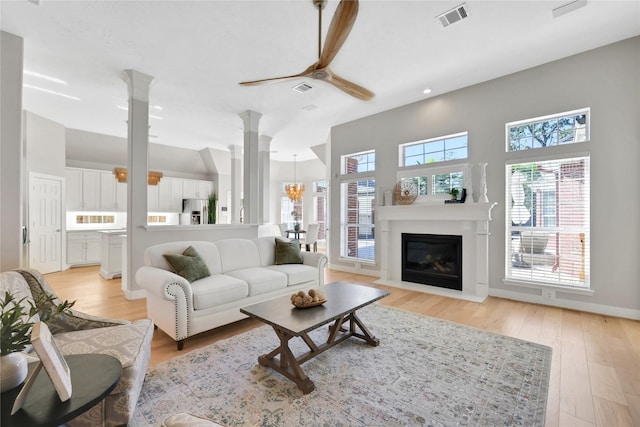 living room featuring ornate columns, light hardwood / wood-style flooring, a wealth of natural light, and ceiling fan